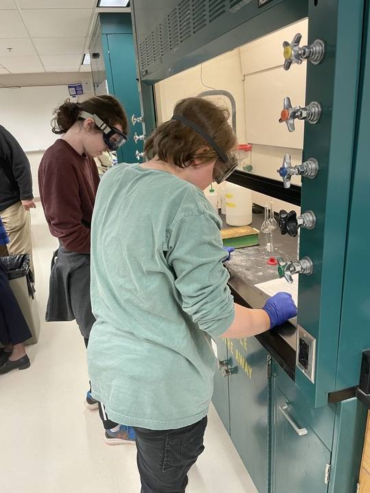 Two students wearing safety goggles, leaning over lab desk